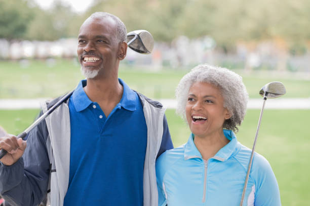 Senior couple laughing together at golf course holding golf clubs Senior couple laughing together at golf course holding golf clubs
